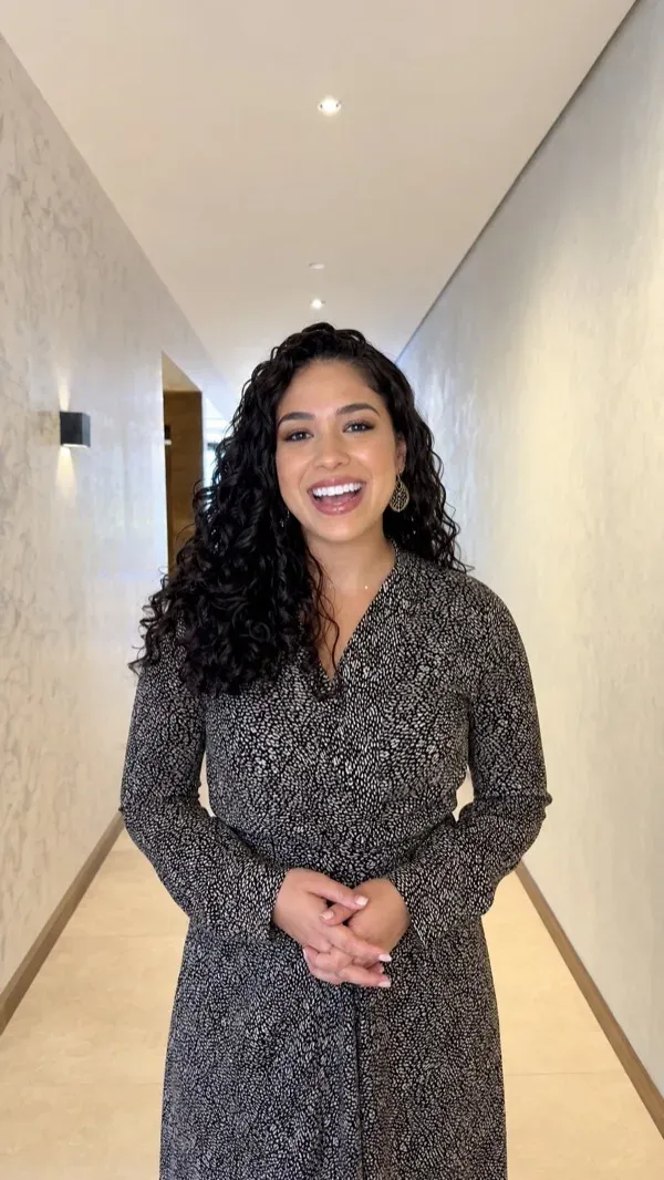 AI avatar in a patterned dress presenting in a softly lit office hallway